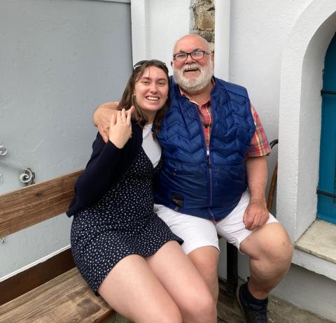 A college aged woman sitting on a bench with an older man with his arm around her shoulder