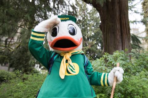 The Oregon Duck mascot holding a hand above its eye while standing in a park