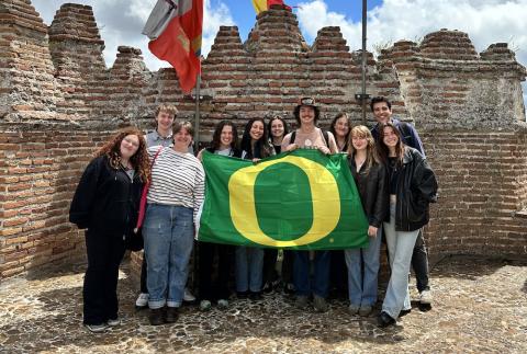 Group of UO students holding a green University of Oregon flag at a medieval castle in Segovia, Spain
