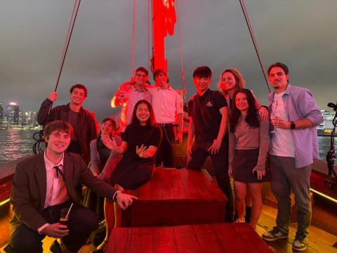 Cohort of ten Global Works Interns smiling on a boat in Hong Kong, China with red LED lighting.