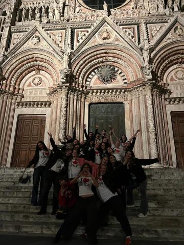 Cohort of students posing with their arms up on the steps of a church in Siena