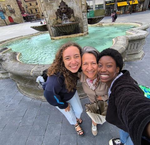 two college aged women taking a selfie with a middle aged woman in front of a fountain