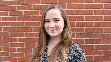 Quinne headshot standing in front of a brick wall