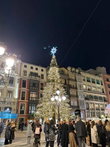 Spanish square with people gathering around a lit Christmas tree at night