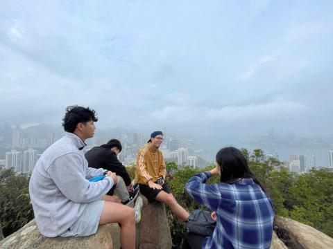 four people sit on rocks at the top of a hike; a foggy cityscape in the background