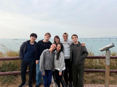 7 students stand together mid-hike; body of water is behind them