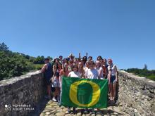 Students stand on an old bridge holding a University of Oregon green and yellow flag.