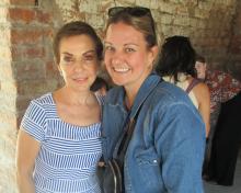 Two women stand in front of a brick wall