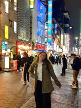 A young woman stands on a busy street in Tokyo at night 