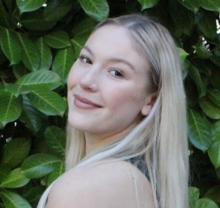 A young woman poses against a leafy background