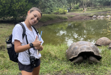 College student posing next to large tortoise.