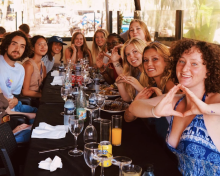 Group of college students at a restaurant table holding up the University of Oregon's hand sign, the letter "O."