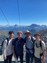 Four college-aged males posing in front of a mountain background. 