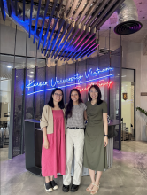 Three females posing in front of a neon sign in Vietnam. 