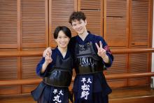 Two young males wearing traditional Japanese Kendo uniforms holding up peace signs. 