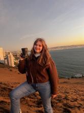 College-aged woman posing on a beach in Chile during sunset holding up a professional camera. 