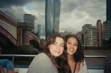 Two people smiling for a photo on a boat with the London skyline, including the distinctive One Blackfriars building, in the background.