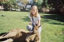 College-aged girl posing behind a kangaroo lying on its back in a park in Australia. 