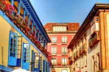 Colorful buildings with balconies adorned with flowers under a clear sky in a town square in Spain.