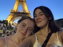 Two people posing for a selfie with the illuminated Eiffel Tower in the background during evening.
