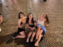 Three people sitting on a cobblestone street at night, smiling and posing for a photo.