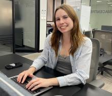 Girl sitting at a desk typing on a computer while smiling for a picture. 
