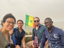 Four people sitting together on a boat with the flag of Senegal visible in the background. They are smiling and appear to be enjoying their time on the water.
