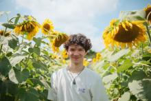 Person smiling in a field of vibrant sunflowers under a clear sky.
