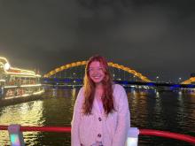 Smiling person on a boat with the Dragon Bridge illuminated in the background in Da Nang, Vietnam at night.