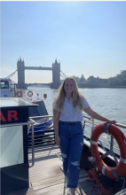 A person standing on a boat with the Tower Bridge in the background on a sunny day.