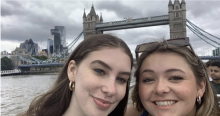 Two girls smiling for a selfie with the London bridge behind them. 