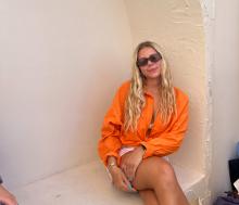 College-aged girl in an orange top wearing sunglasses posing for a picture. 