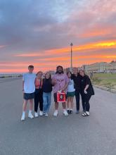 Group of eight friends posing together with a sunset in the background.