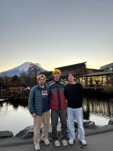 Three individuals posing for a photo with Mount Fuji in the background during sunset.