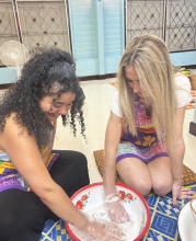 Two people sit on the ground, mixing ingredients together in a bowl