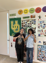 Sara and a friend standing in front of a wall of UO posters and memorabilia, throwing their "O"