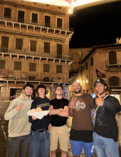 five people stand with a tall building behind them