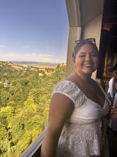 Person in a white dress smiling, standing on a balcony with a scenic view at a historic site in Segovia, Spain.