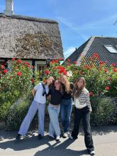 Three girls smiling in front of a bush with flowers. 