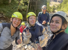 Nathalie and two other program participants wear brightly colored helmets. Rocks and green trees are in the background