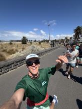 Calvin, in running clothes, a hat, and sunglasses, takes a selfie, with a trail of runners behind him