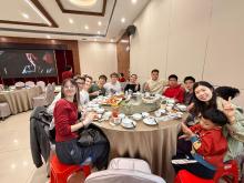 a group of people sit around a large circle table, many dressed in red; they are all smiling and celebrating Chinese New Year