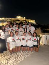 Cohort of GEO students posing for a photo at night wearing matching "I Heart Greece" T-shirts