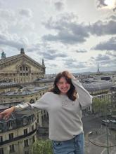 Giana smiling on a rooftop in Paris on a cloudy day with the Eiffel tower in the skyline.