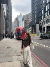 Hana walking down a street in London with a matcha in hand and a red bus in the background