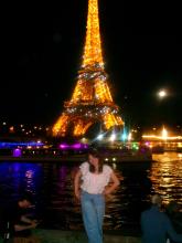 Giana smiling by the River Siene in Paris at night with the Eiffel Tower sparkling in the background
