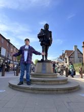 Isaiah standing in front of a William Shakespeare statue in London, holding a staff