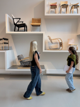 Two students walking in front of a white wall with chairs 
