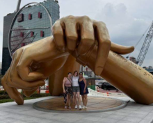Students standing under a golden statue of two hands