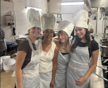 Four UO students with white chef hats smiling in a kitchen